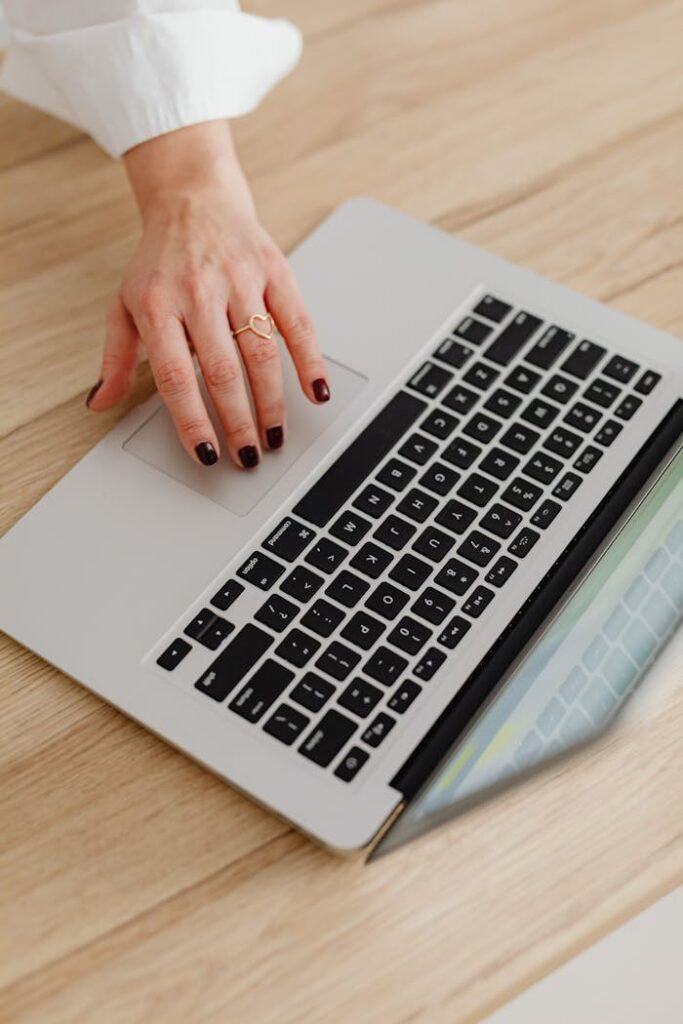 A woman's hand using a laptop touchpad on a wooden desk, showcasing modern technology.